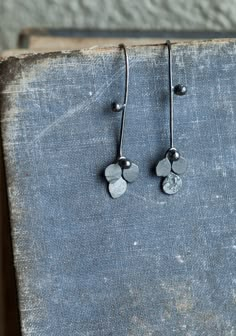 "This is a series which brings me much joy at the moment, light-weight black plant earrings in 925 silver. In this one, playful rivets and kinetic elements create a shape which is organic and abstract while dainty, delicate and beautiful in the ear. An unusual, elegant, delicate botanical pair. Oxidised to black and polished in a rotary tumbler for durability and shine. Subtle contrasts between texture and smoothness, achieved by the careful hammering of the dangles. These are small threader ear Hammered Metal Jewelry, Kinetic Earrings, Earrings Oxidised, Kinetic Jewelry, Organic Earrings, Plant Earrings, Handmade Silver Jewellery, Contemporary Jewelry Design, Botanical Earrings