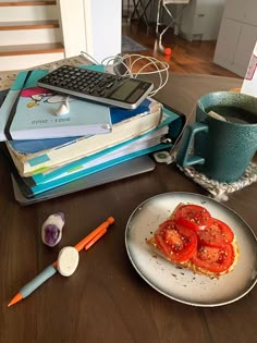 a plate with tomatoes on it next to a stack of books and a cup of coffee