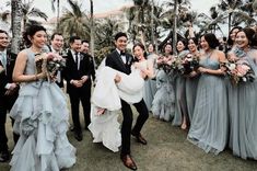 a group of people standing around each other in front of palm trees and holding bouquets