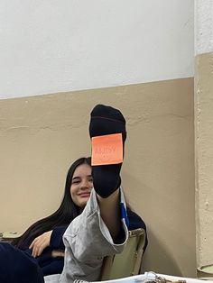 a woman sitting at a table with an orange piece of paper stuck to her head