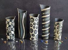 four different vases are lined up on the counter top, one is decorated with black and white designs