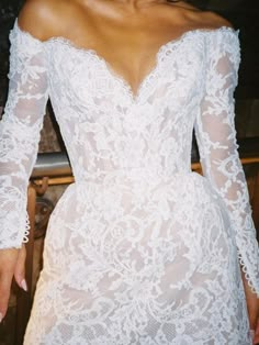 a woman wearing a white dress with long sleeves and an off the shoulder lace top