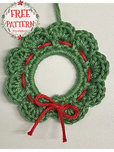 a crochet christmas wreath hanging from a hook on a white wall with the text free pattern below it