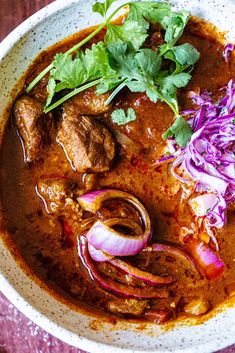 a white bowl filled with meat, onions and cilantro on top of a wooden table