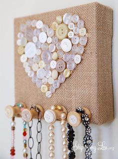 a heart made out of buttons on a burlocked canvas with beads hanging from it