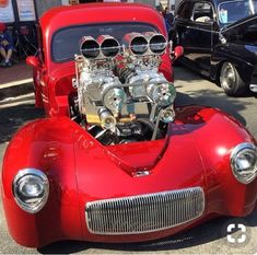 an old red car with the engine in it's hood parked next to other cars