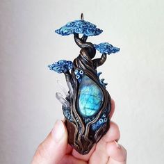 a person holding up a small sculpture with blue decorations on it's sides and an umbrella shaped like a tree