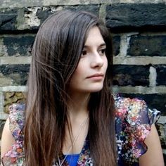 a woman with long hair sitting in front of a brick wall