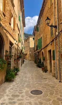 an alley way with stone buildings and green shutters on both sides, surrounded by greenery