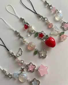 several different types of charms hanging from necklaces on a white surface with one being an apple, the other is a strawberry