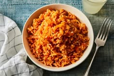 a white bowl filled with rice next to a fork and glass of water on top of a blue table cloth