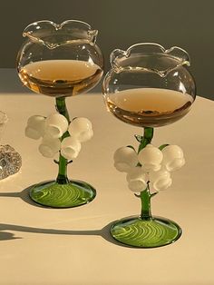 two wine glasses sitting on top of a table next to vases filled with white flowers