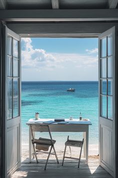 an open door leading to the beach with two chairs and a table in front of it