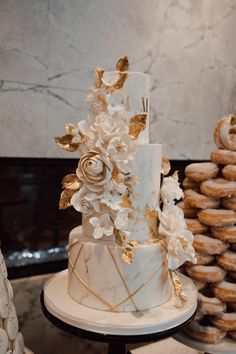 a white and gold wedding cake sitting on top of a table next to donuts