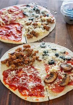 two pizzas sitting on top of a wooden table covered in cheese and toppings