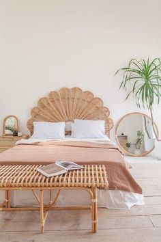 a wicker bed with white sheets and pillows in a bedroom next to a palm tree