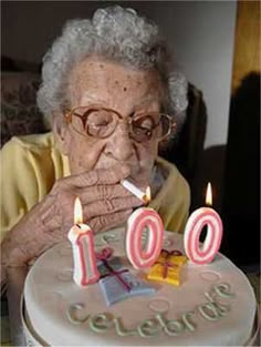 an elderly woman blowing out the candles on her birthday cake that reads 40 years old