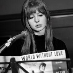 a woman with long hair sitting in front of a microphone and holding a sign that says world without love