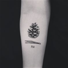 a black and white photo of a pine cone tattoo on the left inner arm with writing underneath it