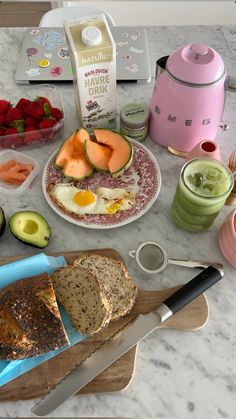 an assortment of breakfast foods on a table with a knife and bowl of strawberries