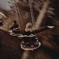 two people riding on swings in an amusement park with blurry image behind them and one person holding onto the strings