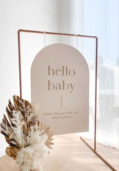 a hello baby sign sitting on top of a table next to a vase filled with flowers