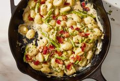 a skillet filled with pasta and vegetables on top of a white counter next to utensils