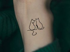 a cat and dog tattoo on the left inner arm, with an outline of two cats sitting next to each other