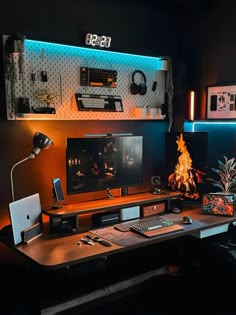 A moody and organized desk setup featuring warm lighting, a central monitor displaying a fire scene, surrounded by tech gadgets and plants. The workspace includes a pegboard organizer with various accessories and modern tech devices. Bedroom Desk Setup, Set Up Pc, Work Wallpaper, Cozy Setup, Trading Room, Earthy Vibes, Gaming Desk Setup, Mac Setup, Cozy Desk