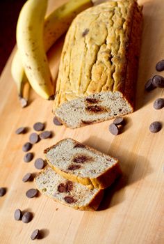 sliced loaf of banana bread with chocolate chips on cutting board next to it and bananas