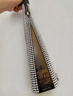 a person is holding a bottle of wine with silver beads on it and the bottle has a black label