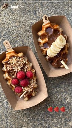 two waffles with bananas, raspberries and chocolate on top are sitting in cardboard boxes