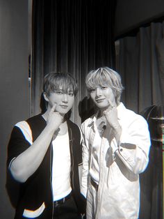 two young men standing next to each other in front of a curtained window with curtains behind them