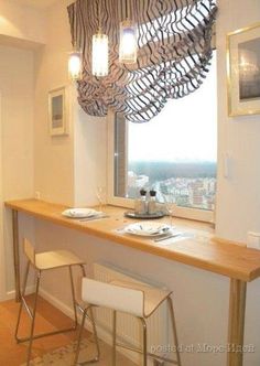 a table with two stools in front of a window and a light fixture hanging from the ceiling