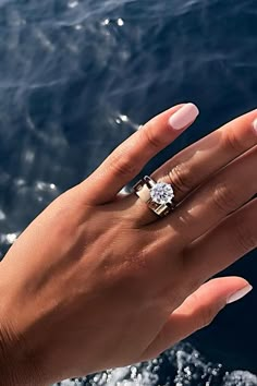 a woman's hand holding a diamond ring over the ocean