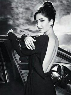 a woman in a black dress leaning on the door of a car