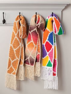 three scarfs hanging from hooks on a wall