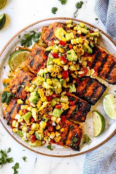 grilled salmon with corn and avocado salsa on a plate next to lime wedges