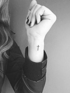 a woman with a small cross tattoo on her left wrist is holding up her hand