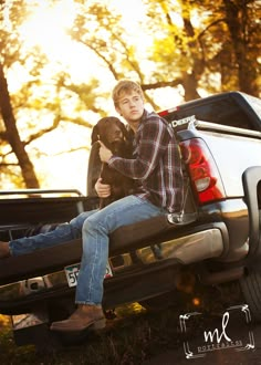 a young man sitting on the back of a pickup truck with his dog in his lap