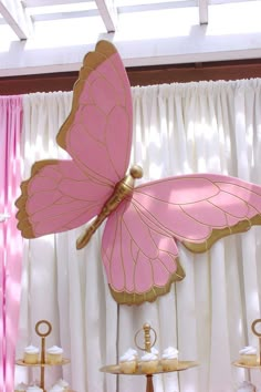 a pink and gold butterfly decoration in front of white drapes on a window sill