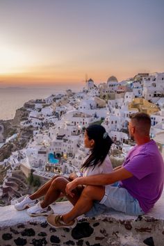 a man and woman sitting on the edge of a cliff looking out at the ocean