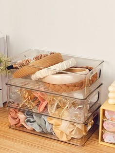 a stack of clear plastic containers filled with different types of clothing and accessories on a wooden floor