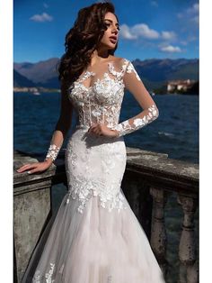 a woman in a white wedding dress standing on a balcony next to the water with her hands on her hips