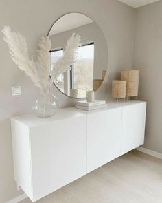 a white dresser with a round mirror on the top and two vases in front of it