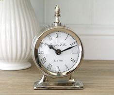 an alarm clock sitting on top of a wooden table next to a vase with flowers