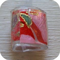 a red and green glass ring with gold accents on it's side sitting on a wooden surface