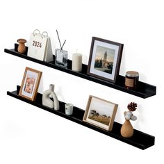 two black shelves with pictures, candles and other items on them in front of a white wall