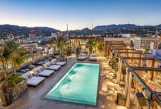 an outdoor swimming pool surrounded by lounge chairs and palm trees at dusk with mountains in the background