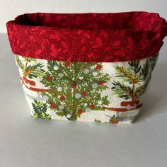 a red and white fabric basket with christmas decorations on the bottom, sitting on a table